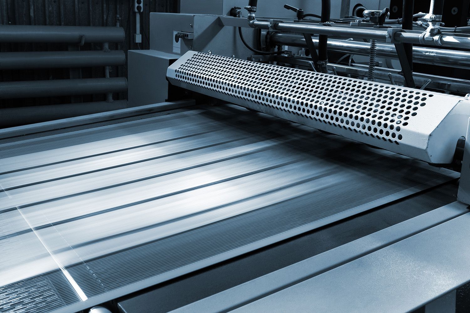 Industrielle Maschine mit Metallwalzen und perforiertem Schutzgitter in einer Fertigungsanlage